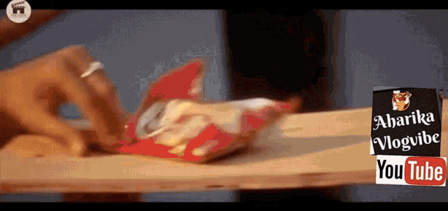 a person is opening a bag of chips on a table with a sign that says ' aharika vlogvibe youtube '