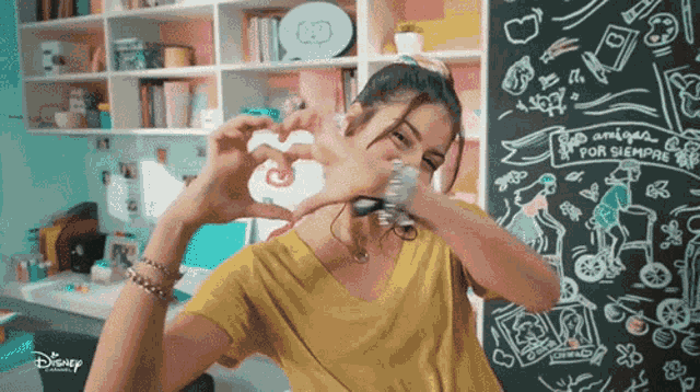a girl is making a heart shape with her hands in front of a blackboard that says amigos por siempre