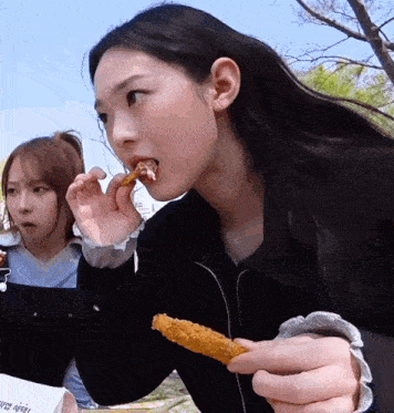 a girl is eating a fried chicken wing with another girl watching