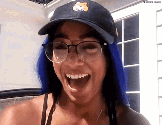 a woman with blue hair and glasses is wearing a hat and laughing .