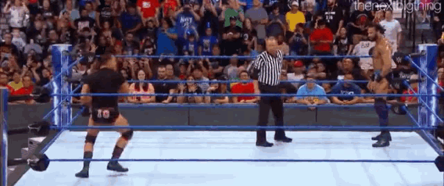 a referee is standing in the middle of a wrestling ring while two wrestlers are fighting in front of a crowd .