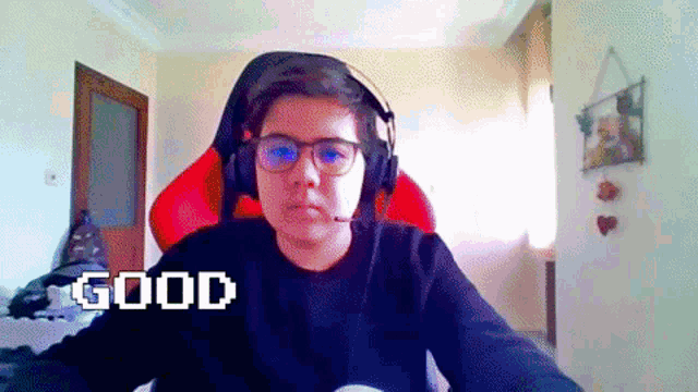a boy wearing headphones and glasses is sitting in a red chair and says good