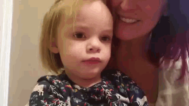 a woman is holding a little girl who is looking at the camera .