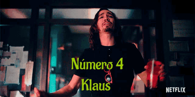 a man wearing a number 4 klaus t-shirt stands in front of a window