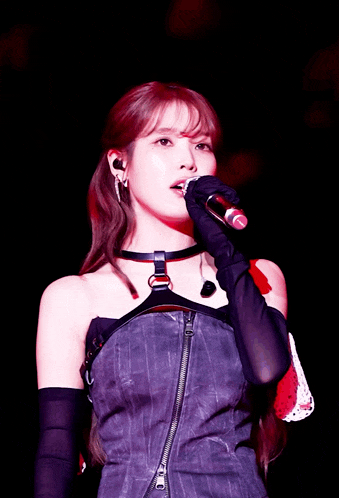 a woman singing into a microphone wearing black gloves and a choker