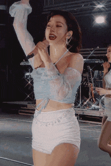 a woman in a blue top and white shorts is singing into a microphone .