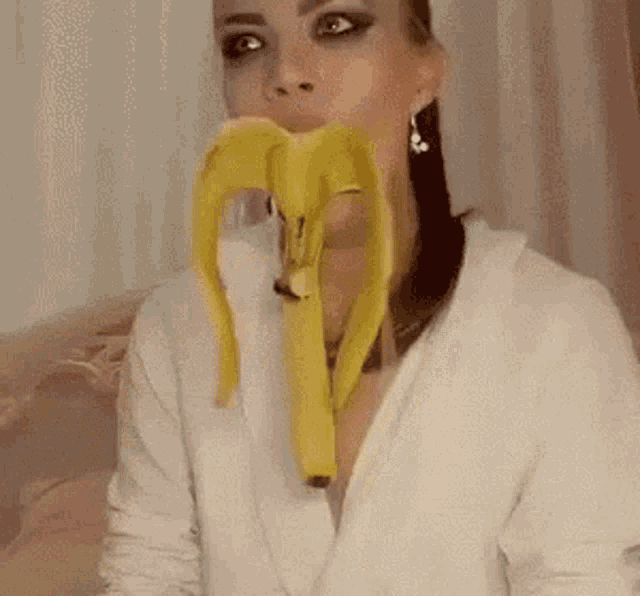 a woman is eating a banana with her mouth open while sitting on a bed .