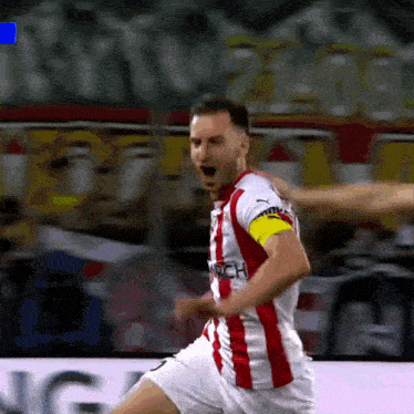 a soccer player wearing a red and white jersey with a yellow armband that says ' ntech ' on it