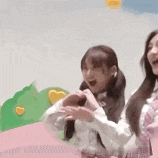 a girl is making a heart shape with her hands while standing next to another girl .