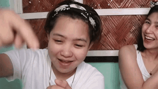 a woman wearing a headband is smiling while another woman laughs behind her