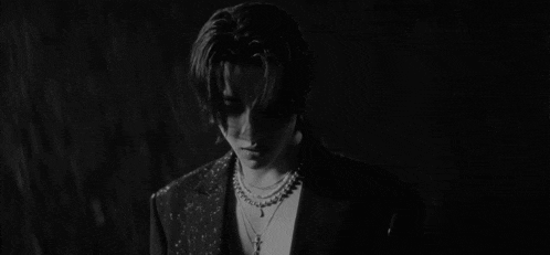 a black and white photo of a young man wearing a necklace .