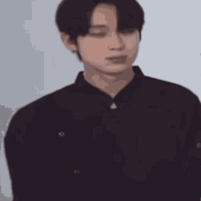 a young man wearing a black shirt is standing in front of a white wall .