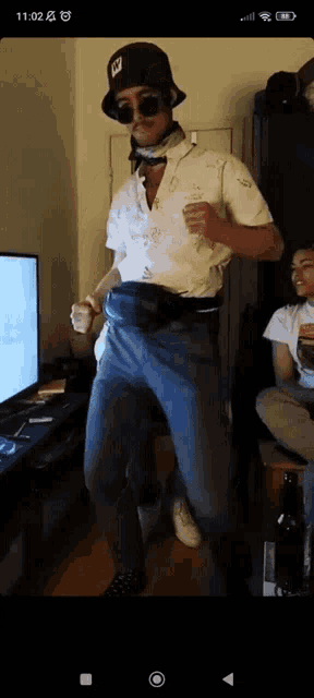 a man in a hat and sunglasses is dancing in a room