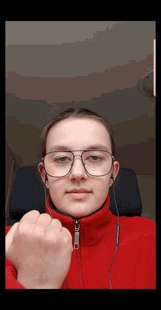 a young woman wearing glasses and a red jacket holds her fist up