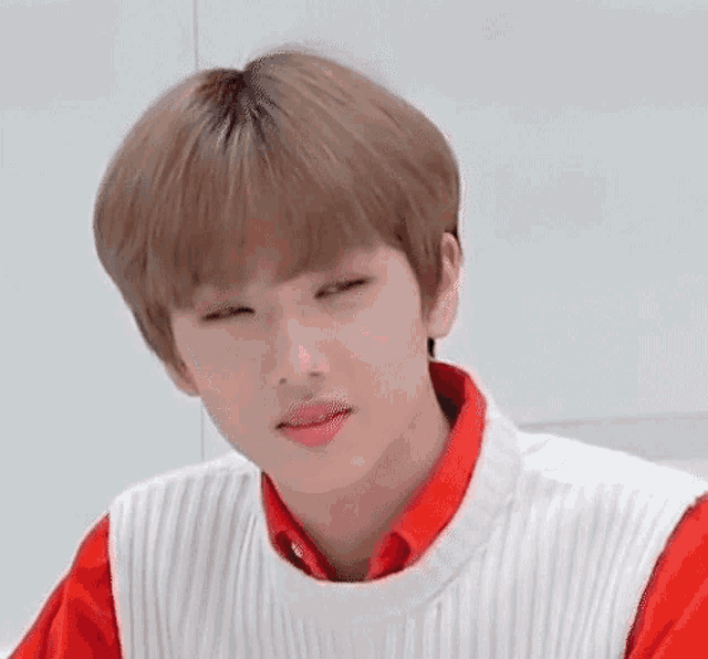 a young man wearing a red shirt and a white sweater is making a funny face .