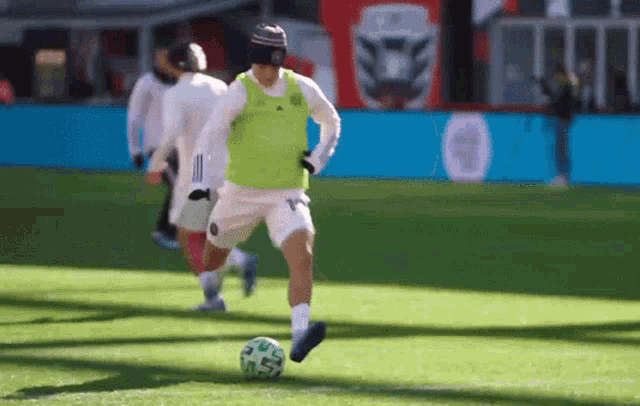 a man in a green vest is kicking a soccer ball on a soccer field