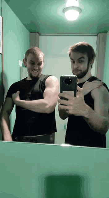 two men are taking a picture of themselves in a bathroom mirror