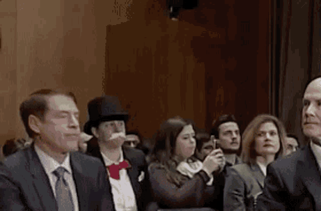 a group of people are sitting in a room and one of them is wearing a top hat and a bow tie .
