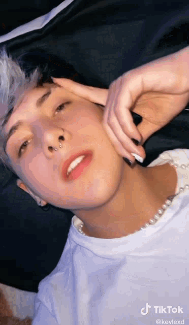 a young man with a nose ring is laying down with his hand on his face