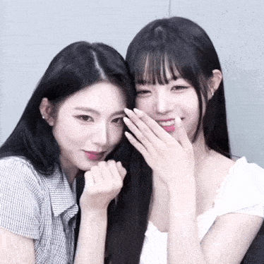 a couple of girls standing next to each other with one covering her mouth with her hand