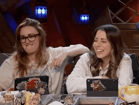 two women are sitting at a table with their arms around each other laughing