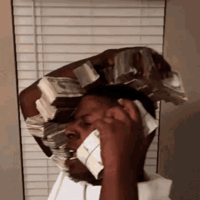 a man is talking on a cell phone with a stack of money on his head