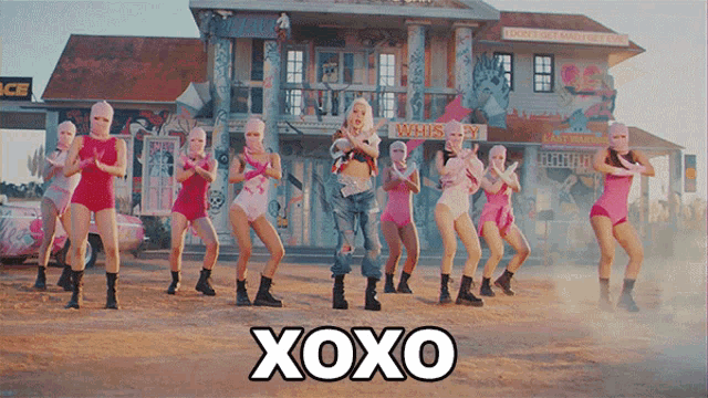 a group of women are dancing in front of a building that says xoxo