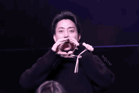 a man in a black sweater making a heart shape with his hands