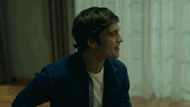 a man in a blue shirt and white t-shirt is sitting in front of a window