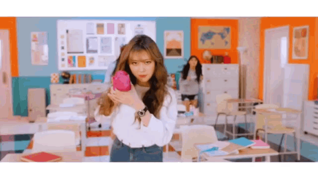 a girl in a classroom is holding a pink object in her hand