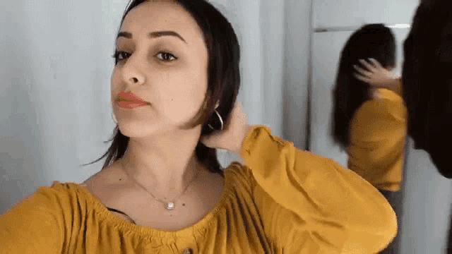 a woman in a yellow shirt is touching her hair in front of a mirror .