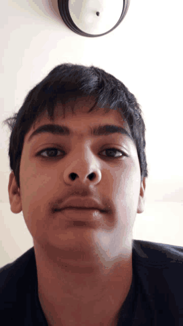 a close up of a young man 's face with a clock behind him