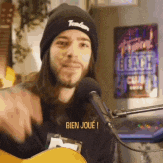 a man wearing a black beanie and a shirt that says bien joue is singing into a microphone