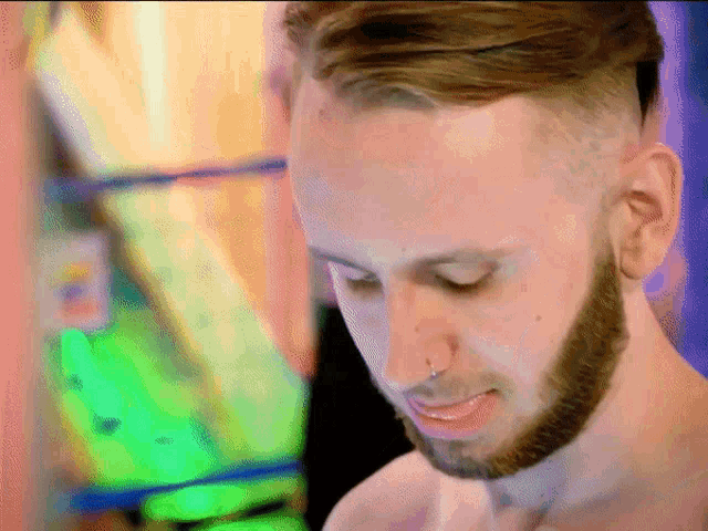 a shirtless man with a beard and nose ring looks down