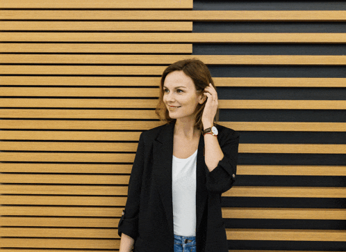 a woman wearing a black jacket and a white shirt is standing in front of a wooden wall