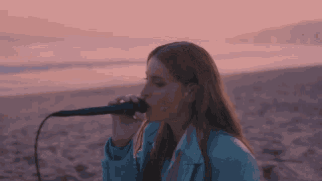 a woman singing into a microphone on the beach at sunset