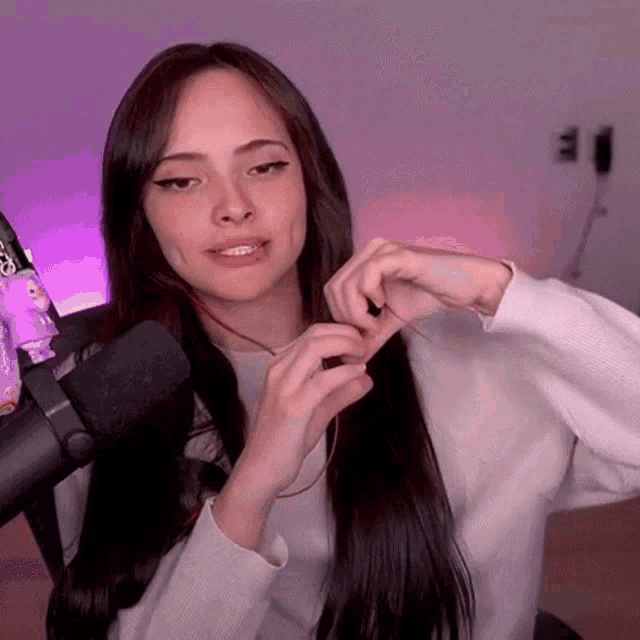 a woman with long hair is sitting in front of a microphone and making a heart shape with her hands