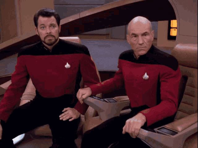two men are sitting next to each other and one has a badge on his shirt that says ' captain '