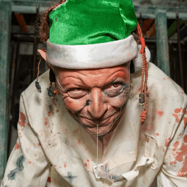 a man wearing a green santa hat and a white shirt with blood coming out of his mouth