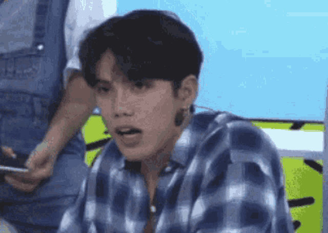 a young man wearing a plaid shirt and earrings is making a funny face .