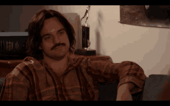a man with long hair and a mustache is sitting in front of a trophy