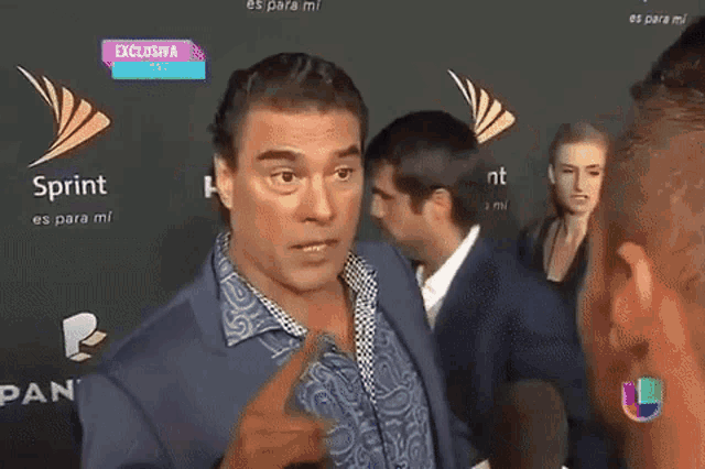 a man in a suit is talking to another man on a red carpet in front of a sprint logo .