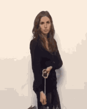 a woman in a black sweater is holding an umbrella in front of a white wall .