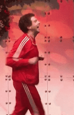 a man in a red jacket and red pants is dancing in front of a christmas tree .