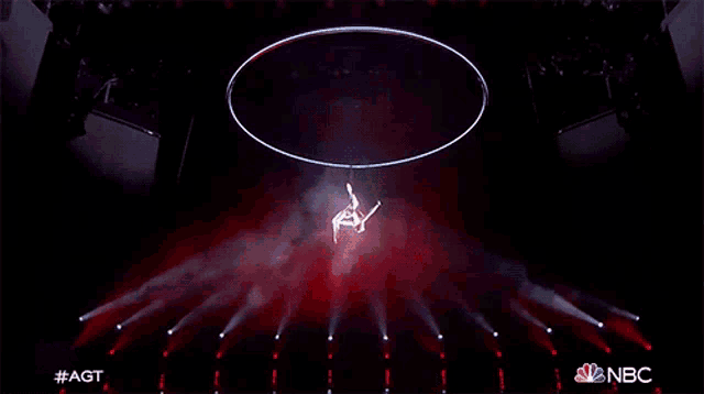 a performer is hanging from a hoop on a stage with nbc written on the bottom