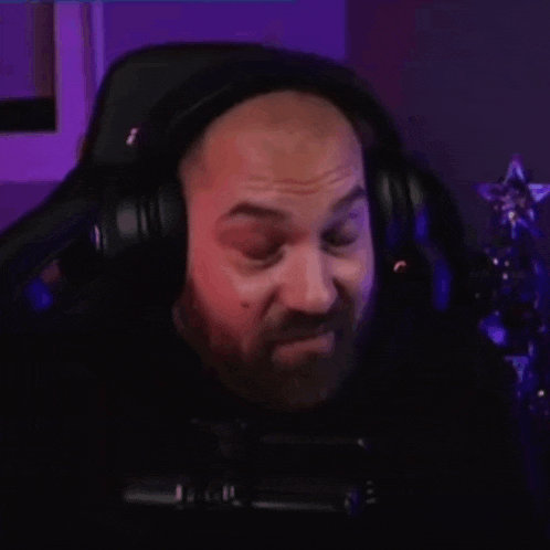 a bald man with a beard wearing headphones is sitting in front of a microphone .