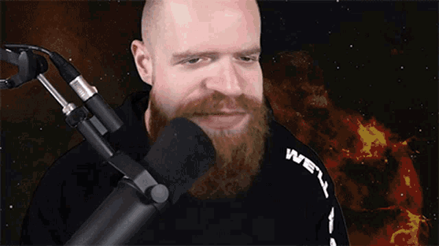 a man with a beard is standing in front of a microphone and wearing a black shirt that says wefly