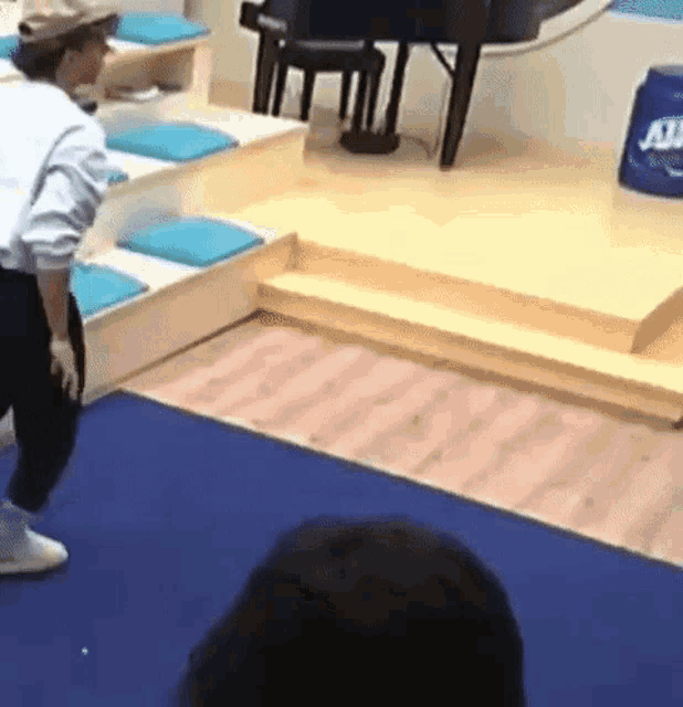 a man in a hat is standing on a blue rug in a room with stairs .