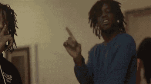 two men with dreadlocks are standing next to each other in a room . one of the men is pointing at the camera .