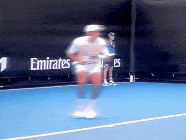 a blurred image of a tennis player on a blue court with an emirates banner behind him
